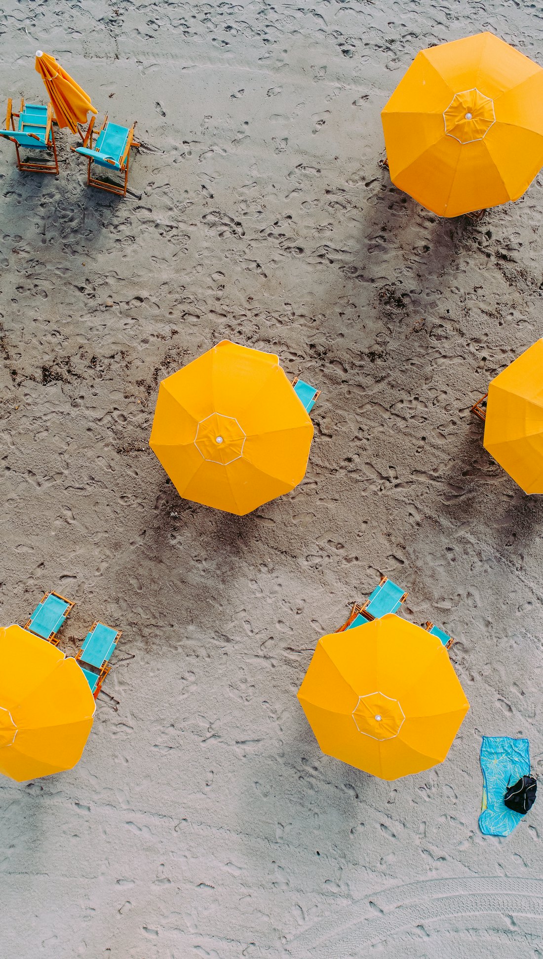 Bright yellow beach umbrellas and turquoise deck chairs on golden sand, seen from above